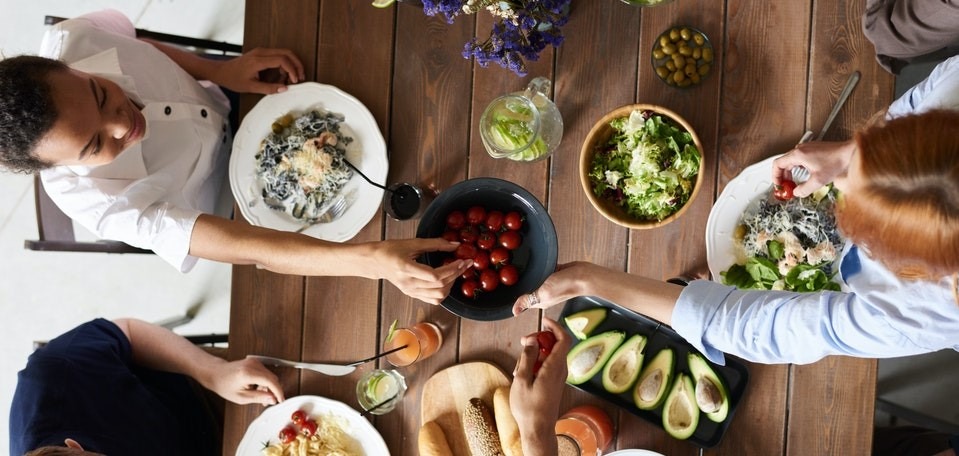 Dieses Bild zeigt Freunde, die an einem Tisch sitzen und gemeinsam eine gesunde Mahlzeit essen.