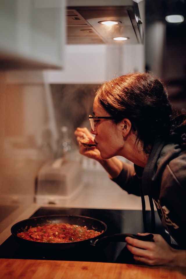 Das Foto zeigt eine Frau, die ihr selbst gekochtes Essen, einen Gemüseeintopf, abschmeckt