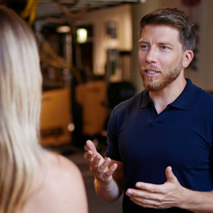 Personal Trainer und Sportwissenschaftler Martin Fiedler steht im Fitnessstudio einer Klientin gegenüber und coacht sie.