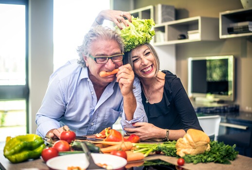 Auf diesem Bild sieht man ein älteres Paar, welches sichtlich Spaß beim Kochen und mit ihrer gesunden Ernährung hat.