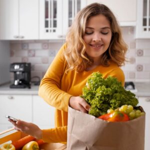 Dieses Bild zeigt eine Frau, die ihren Einkauf an gesunden Lebensmitteln in Ihrer Küche auspackt. In diesem Blog-Artikel erfahren Sie 5 Tricks wie Sie in Ihrem Alltag automatisch gesünder essen.