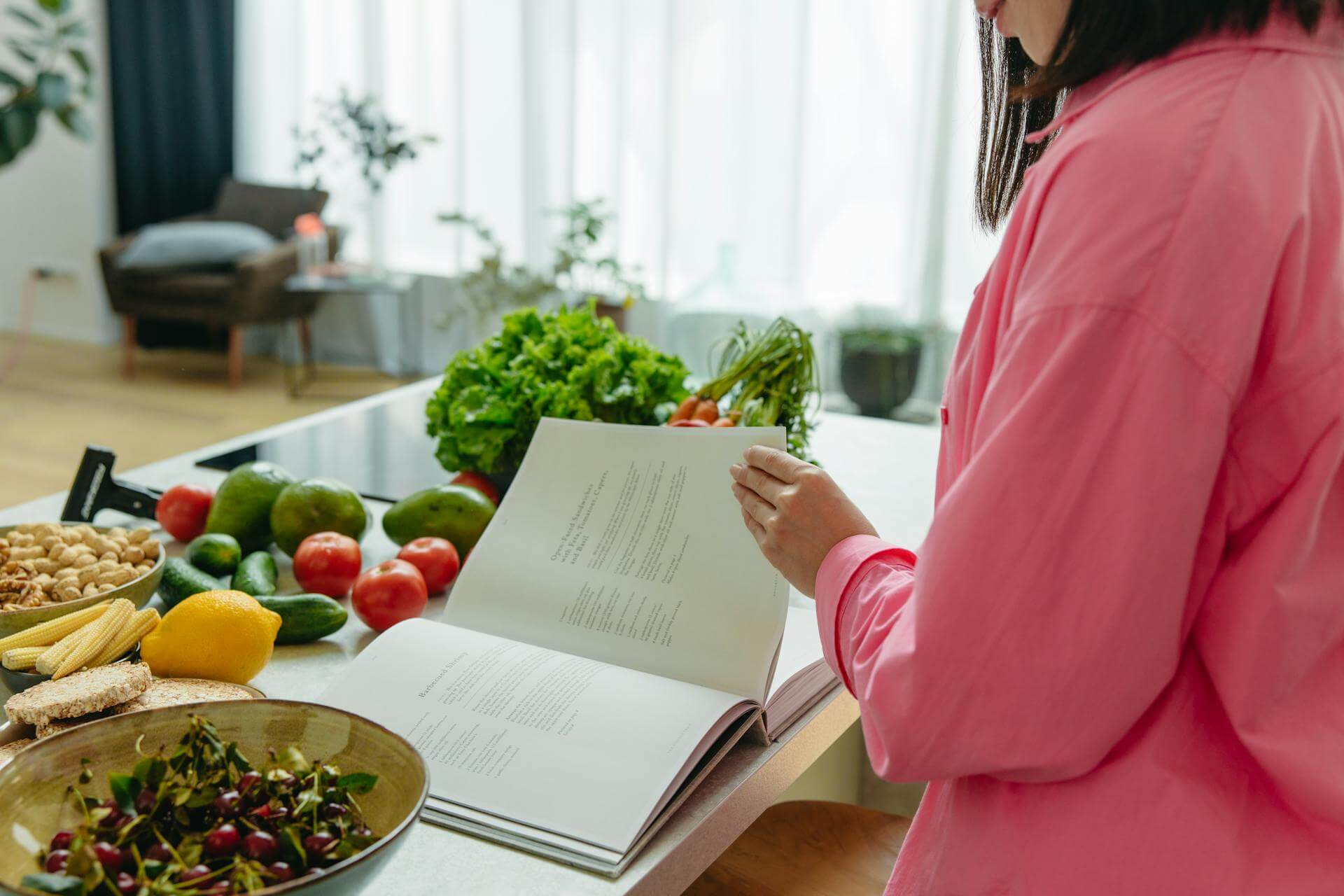 Dieses Foto zeigt eine Frau beim Kochen. Sie blättert in einem Kochbuch, um neue Ideen zu gewinnen. Um sie herum stehen gesunde Lebensmittel.